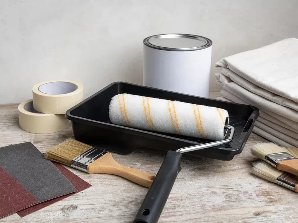 Rodillo, brochas, bandeja y accesorios de pintura ordenados en una mesa
